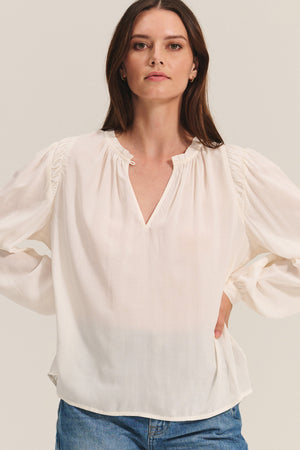 A woman faces forward in the TAMARA BLOUSE by Velvet by Graham & Spencer—a feminine rayon challis top with a v-neckline—paired with light blue jeans against a neutral background.