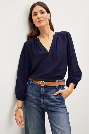 A woman wearing relaxed fit jeans and an ASHLEY V-NECK TOP by Velvet by Graham & Spencer.