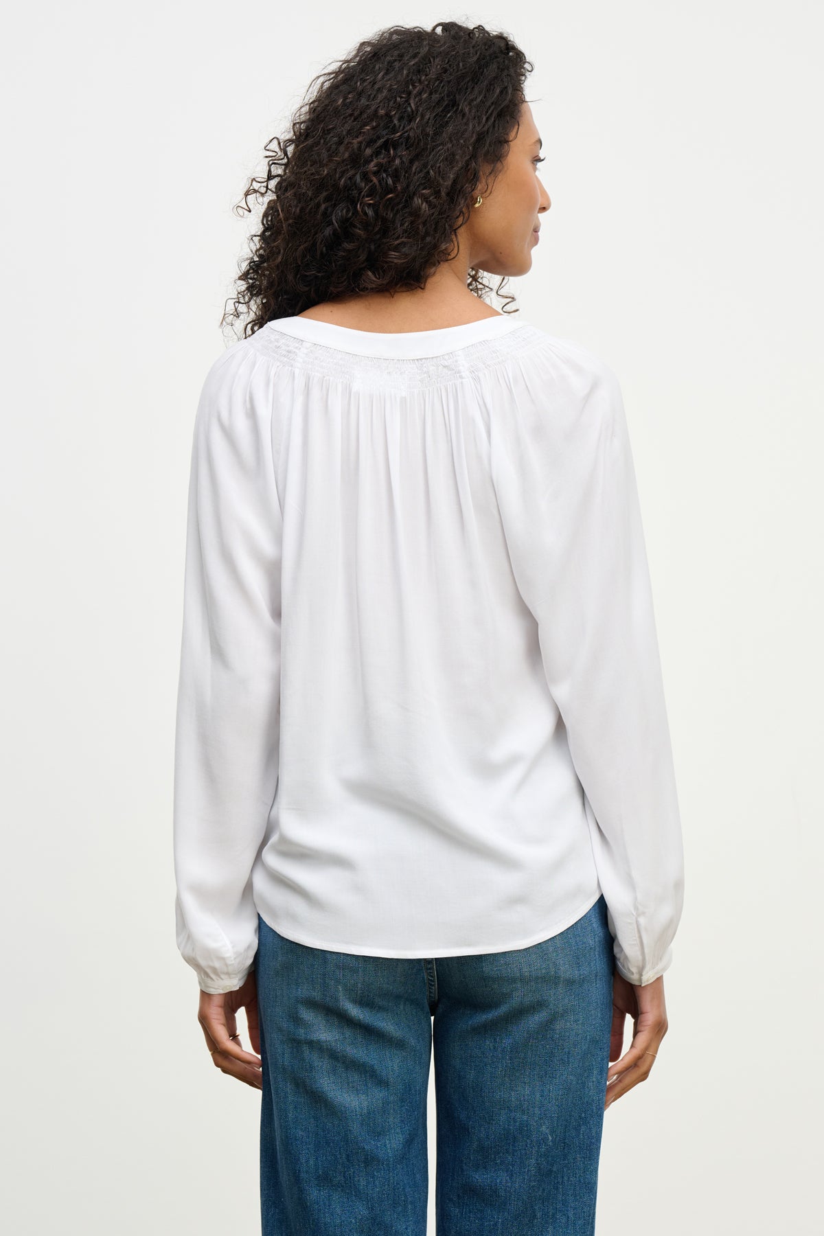 A woman stands with her back to the camera, wearing the AURELIA TOP by Velvet by Graham & Spencer—a breathable rayon challis long sleeve top—paired with blue jeans against a plain light background.-40227028795585