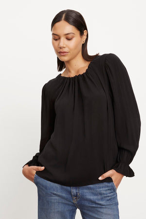 The model is wearing a Velvet by Graham & Spencer BRISTOL NECK TIE TOP, a luxurious black blouse with pleated sleeves, made from rayon challis fabric.