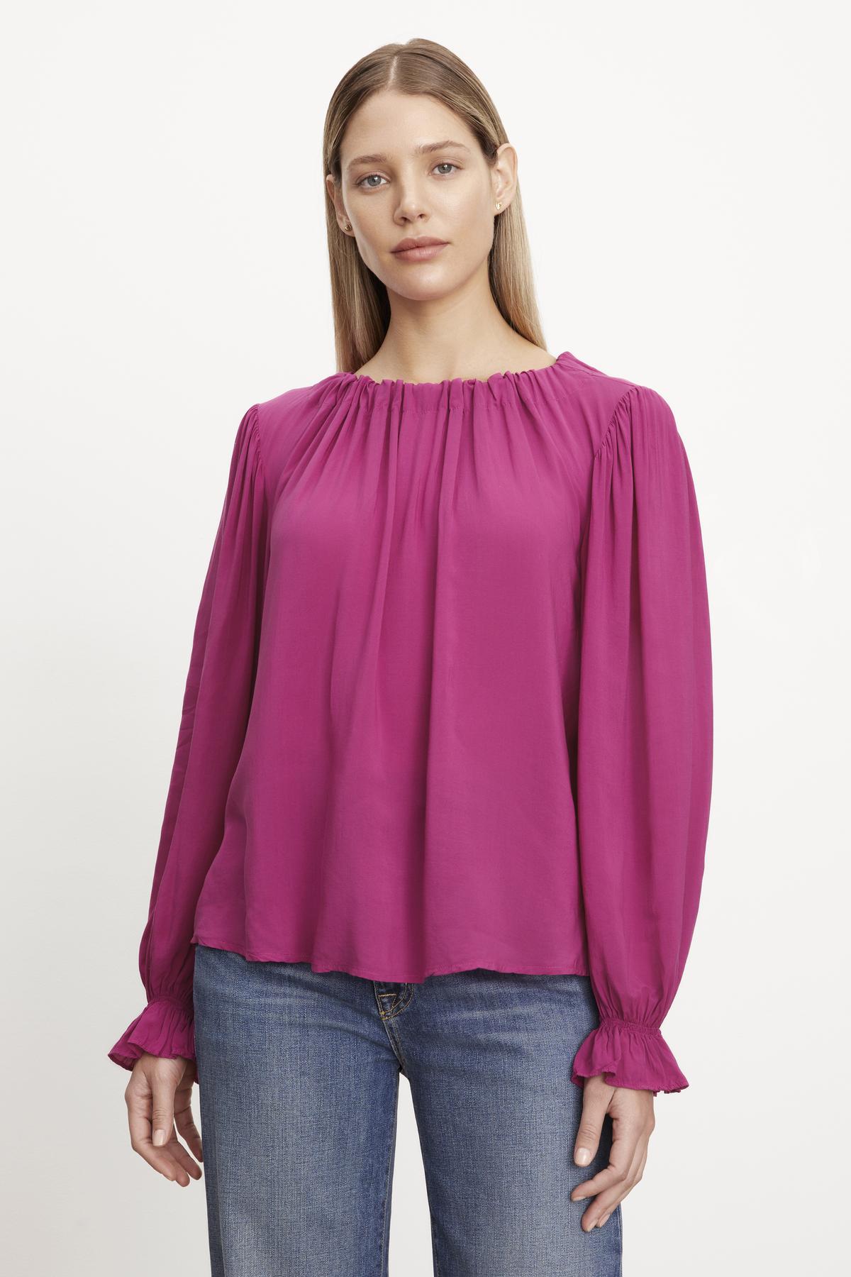 A woman wearing the BRISTOL NECK TIE TOP by Velvet by Graham & Spencer, paired with blue jeans, stands against a white background.-37618504728769