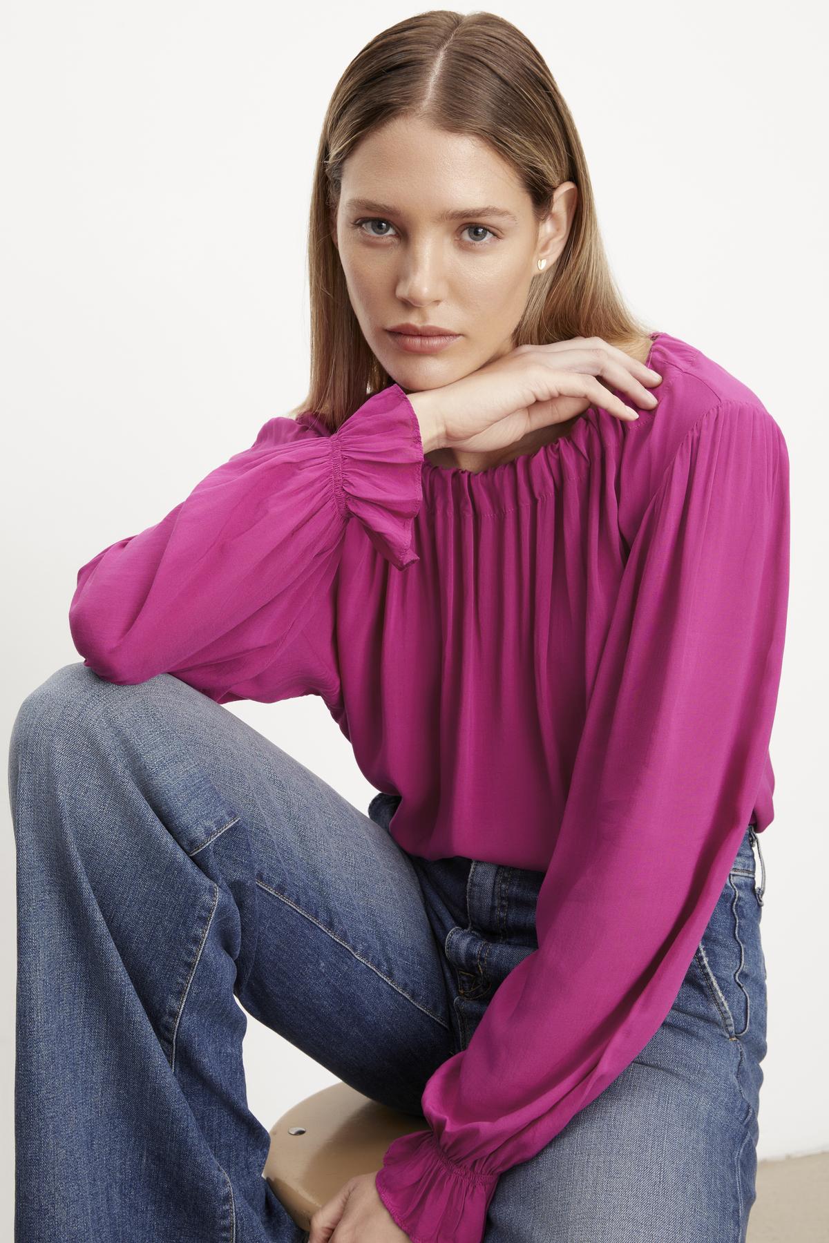   The model is wearing a luxurious Velvet by Graham & Spencer pink Bristol Neck Tie Top made of rayon challis fabric and paired with jeans. 