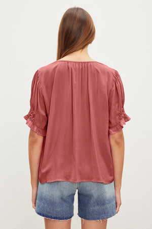 A person with long hair is seen from the back, wearing a CALISSA SPLIT NECK BLOUSE by Velvet by Graham & Spencer and blue denim shorts.