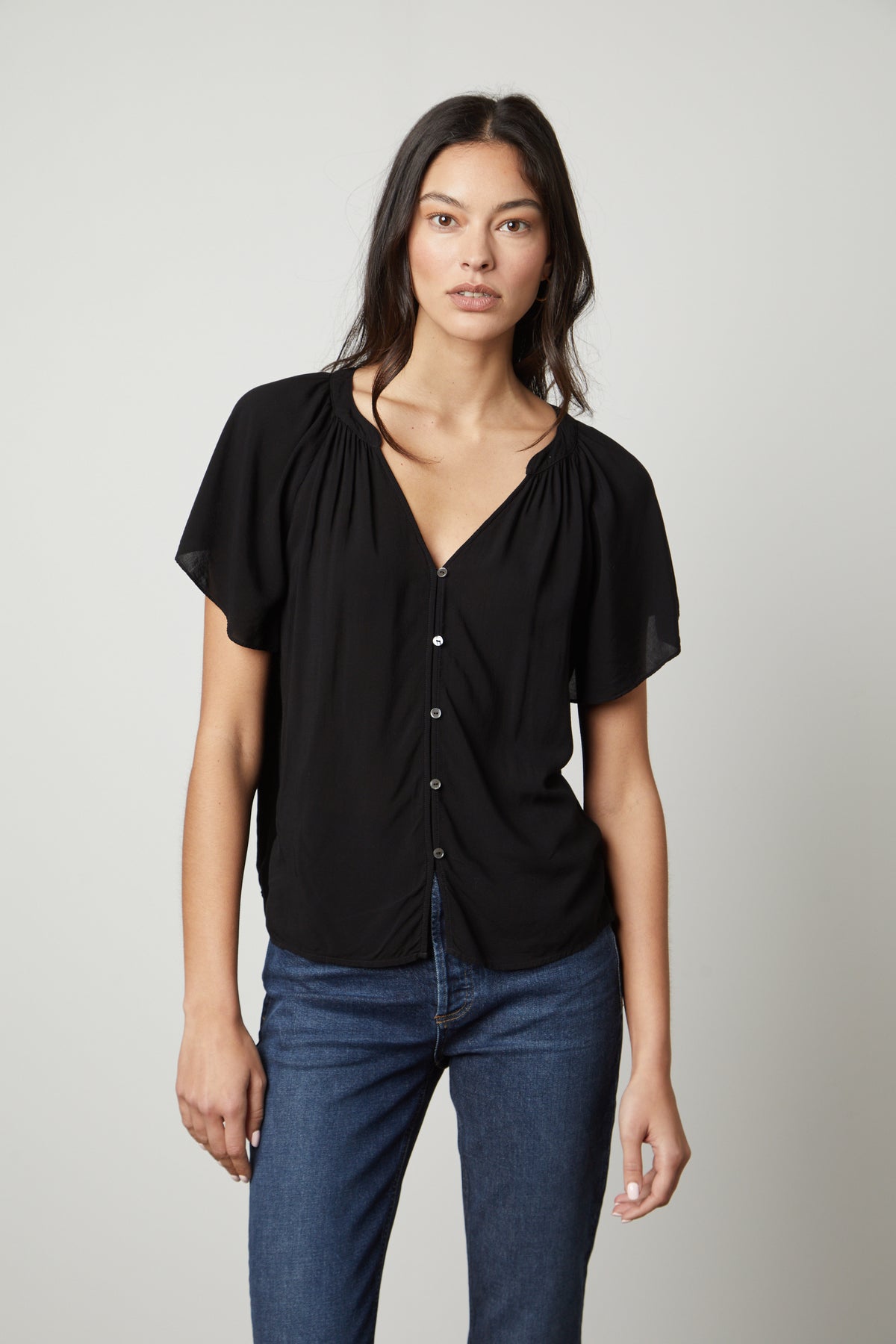   The model is wearing jeans and a Velvet by Graham & Spencer HARLEY FLUTTER SLEEVE TOP in black 