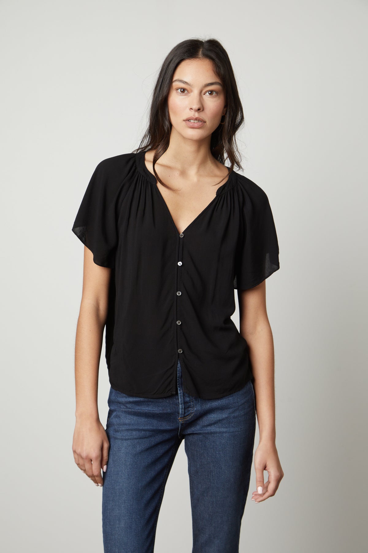 The model is wearing jeans and a Velvet by Graham & Spencer HARLEY FLUTTER SLEEVE TOP in black-26727735492801