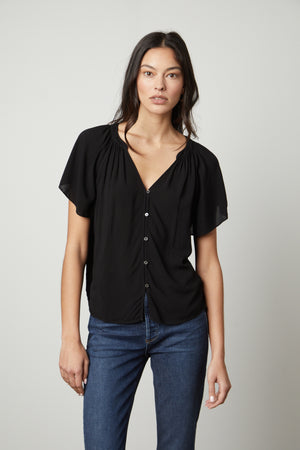 The model is wearing jeans and a Velvet by Graham & Spencer HARLEY FLUTTER SLEEVE TOP in black