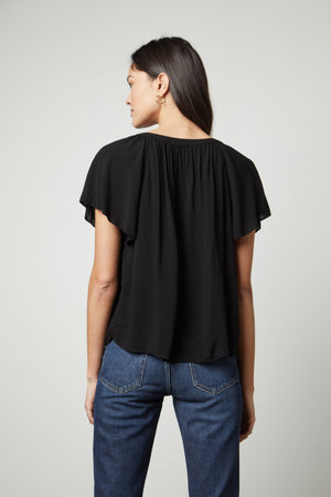 The back view of a woman wearing a Velvet by Graham & Spencer HARLEY FLUTTER SLEEVE TOP and jeans.