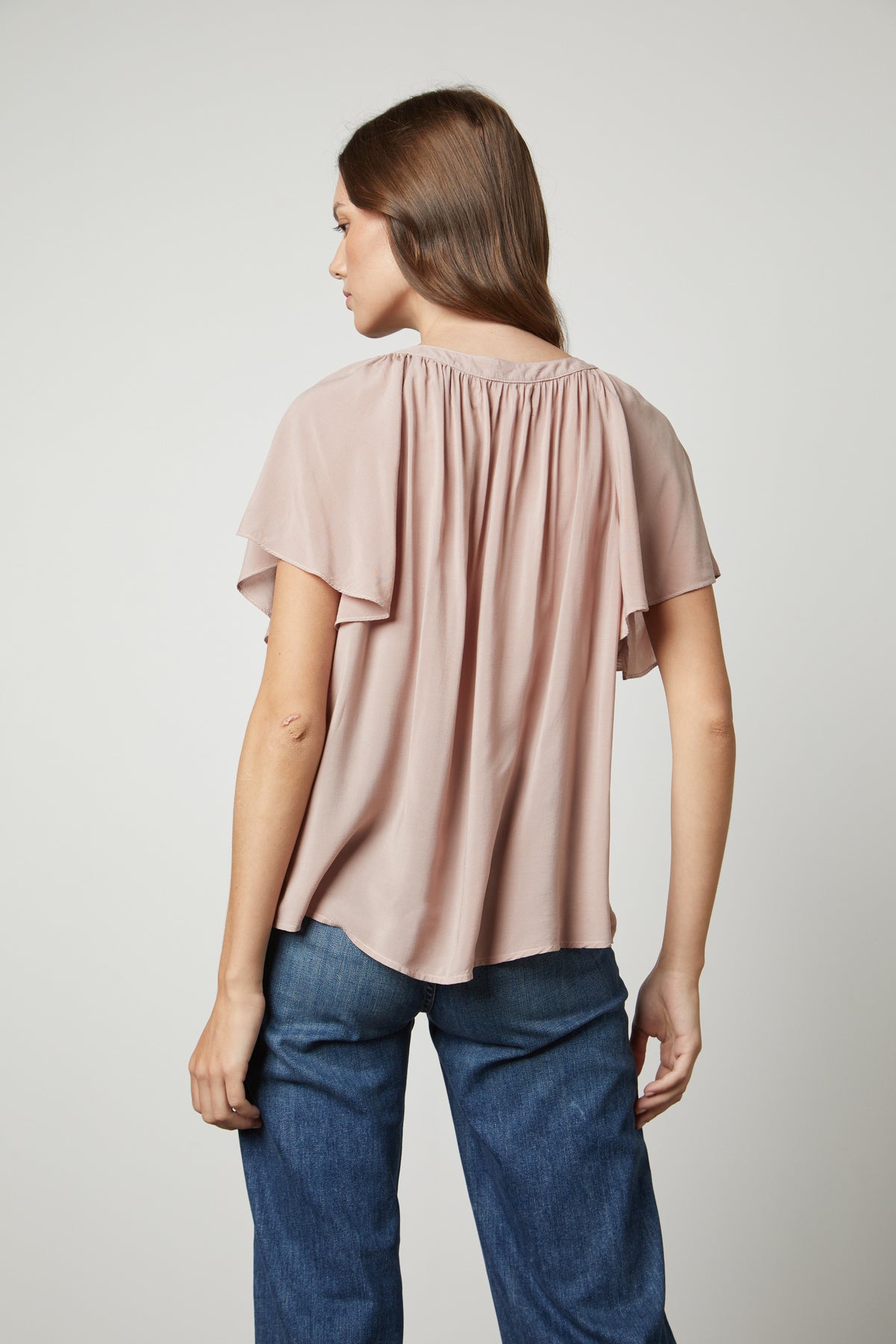 The back view of a woman wearing jeans and a HARLEY FLUTTER SLEEVE TOP by Velvet by Graham & Spencer.-26727733559489