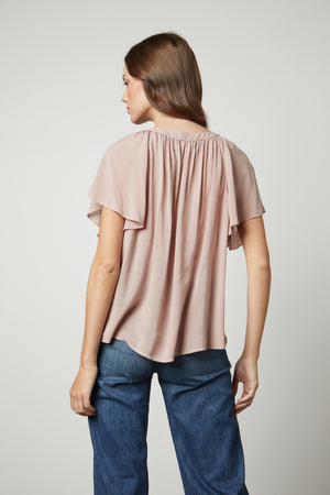 The back view of a woman wearing jeans and a HARLEY FLUTTER SLEEVE TOP by Velvet by Graham & Spencer.