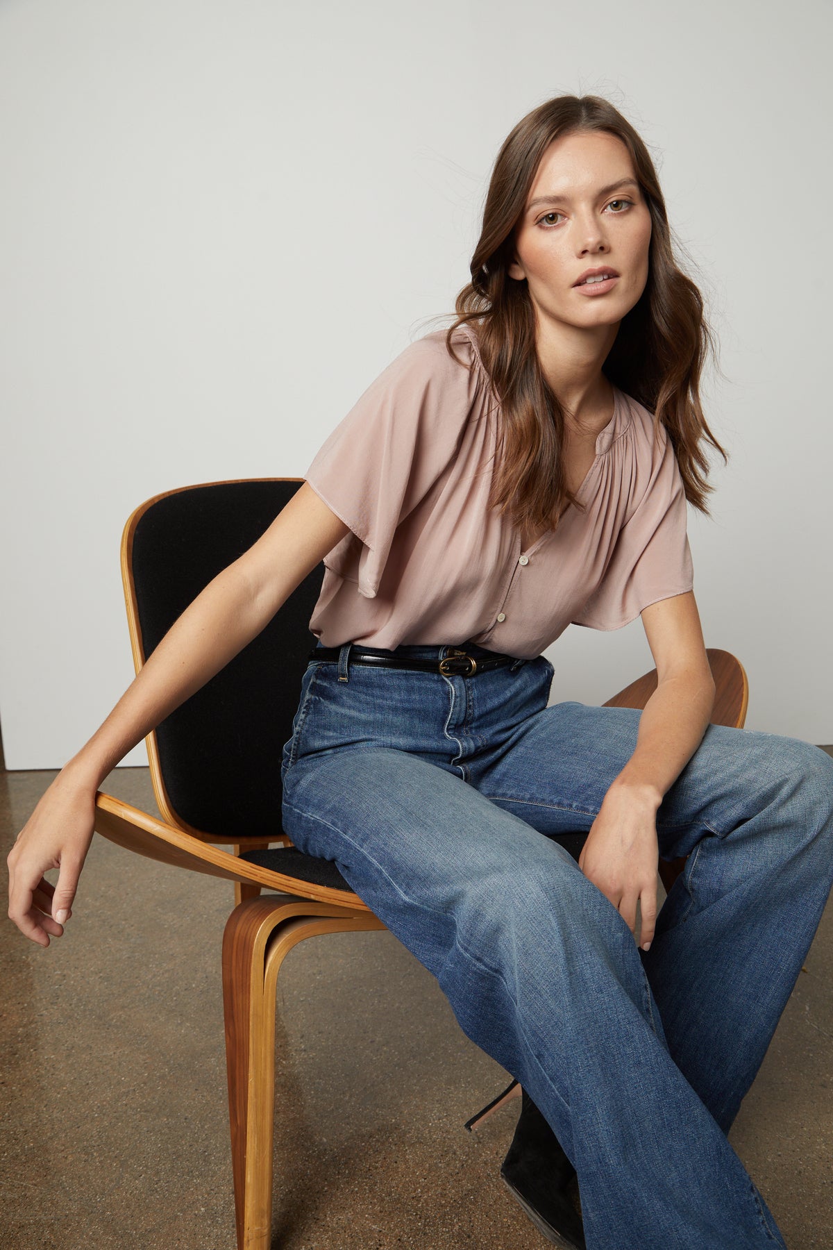   A woman is sitting on a chair wearing jeans, belt, and a pink Velvet by Graham & Spencer HARLEY FLUTTER SLEEVE TOP. 