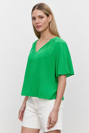 The model is wearing a JAYCEE SPLIT NECK BLOUSE by Velvet by Graham & Spencer and white shorts.