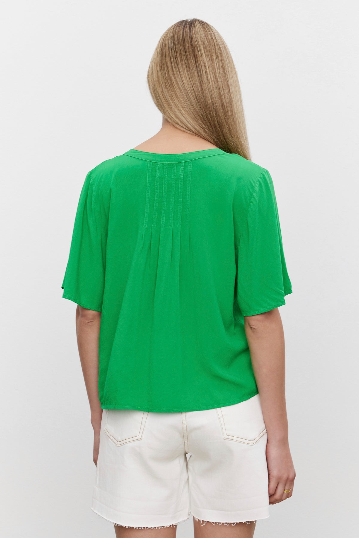   The woman, with a relaxed silhouette, is seen from the back, wearing a Velvet by Graham & Spencer JAYCEE SPLIT NECK BLOUSE and white shorts. 