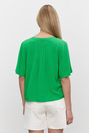 The woman, with a relaxed silhouette, is seen from the back, wearing a Velvet by Graham & Spencer JAYCEE SPLIT NECK BLOUSE and white shorts.