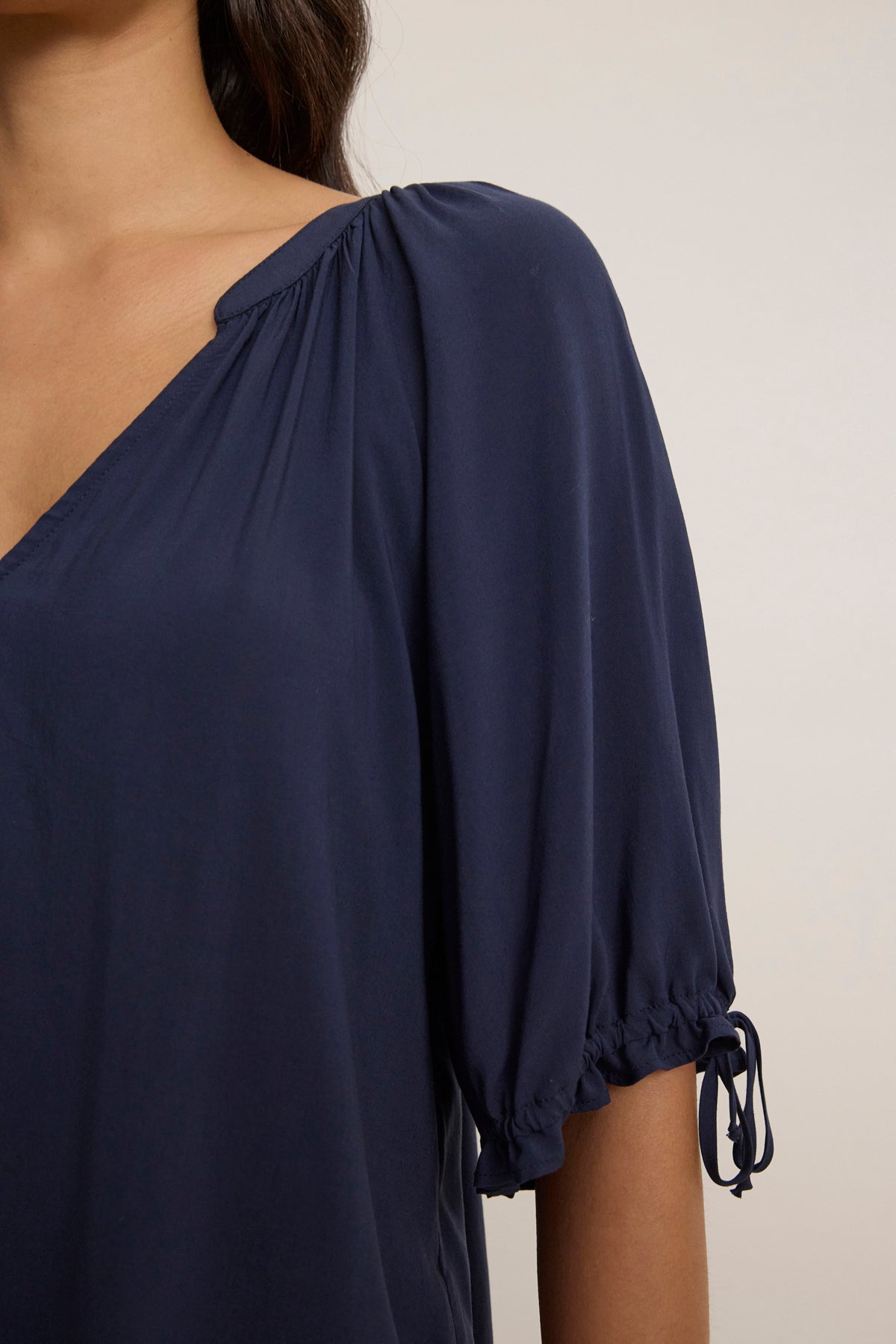 A person wearing the LUNA TOP by Velvet by Graham & Spencer—a relaxed-fit, navy blue top with short gathered sleeves and a V-neck—is shown from the shoulders down.-39148730384577