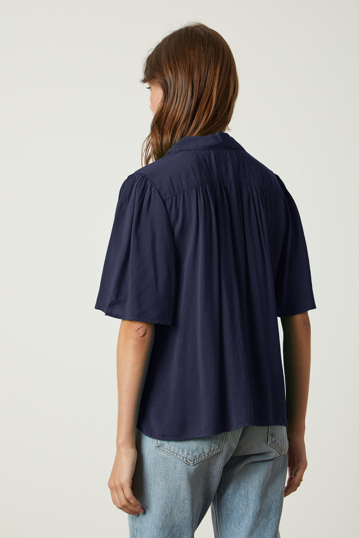   The back view of a woman wearing a Nikki button-up top by Velvet by Graham & Spencer with pleats. 