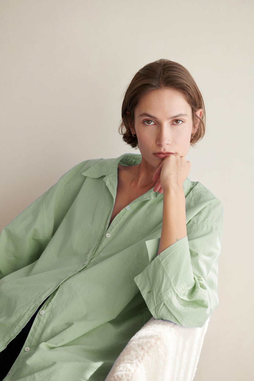 A woman is sitting on a chair in an oversized Velvet by Jenny Graham REDONDO BUTTON-UP SHIRT.