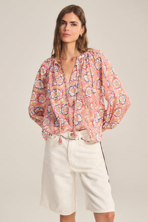 A woman models the REESE TOP by Velvet by Graham & Spencer—a lightweight cotton top with puffed sleeves and a tie-neck—paired with white knee-length shorts, standing against a plain background.