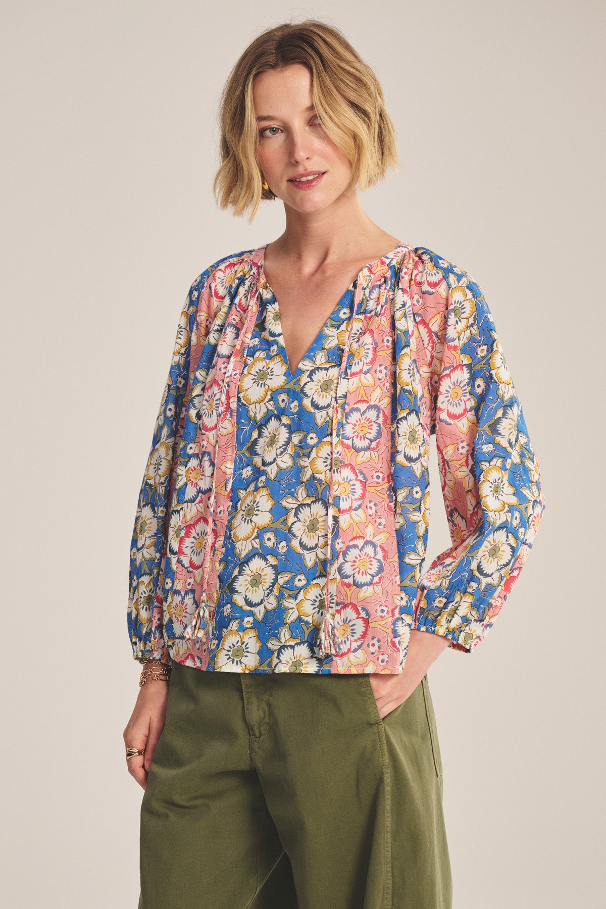 Wearing the REESE TOP by Velvet by Graham & Spencer—a lightweight printed cotton piece with puffed sleeves and a V-neckline—paired with olive green pants, standing against a neutral background.