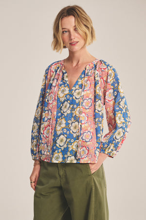 Wearing the REESE TOP by Velvet by Graham & Spencer—a lightweight printed cotton piece with puffed sleeves and a V-neckline—paired with olive green pants, standing against a neutral background.
