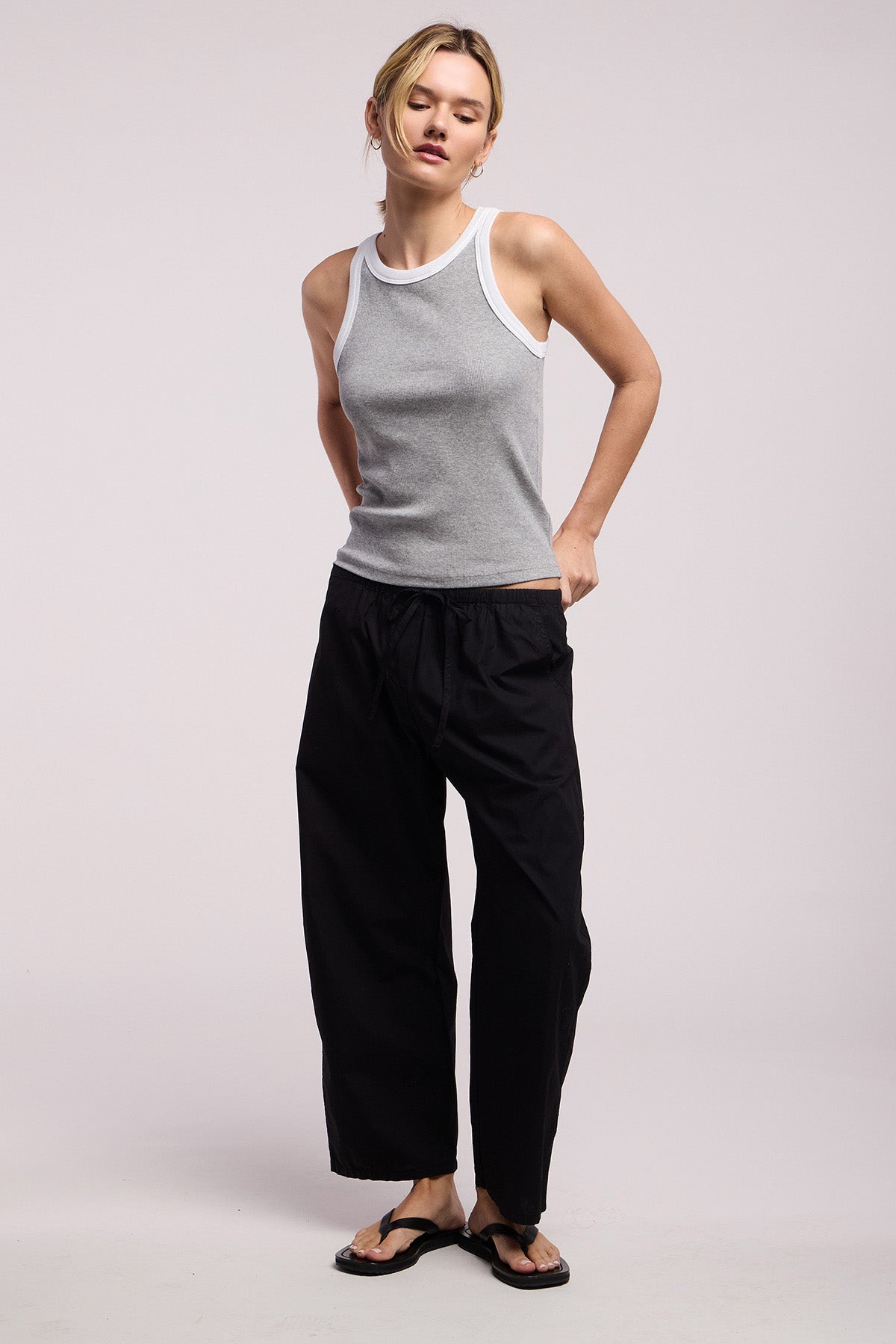 A person wearing a gray sleeveless top, the ALLEGRA PANT by Velvet by Graham & Spencer—black, wide barrel leg and cropped—and black sandals stands against a plain light background.-41370867073217