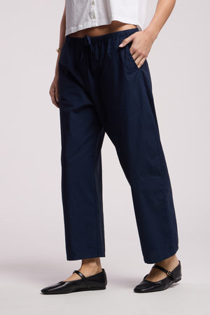 Wearing the ALLEGRA PANT by Velvet by Graham & Spencer—loose-fitting navy cropped barrel leg pull-on pants—with a white cropped shirt and black flats, one hand casually in a pocket.