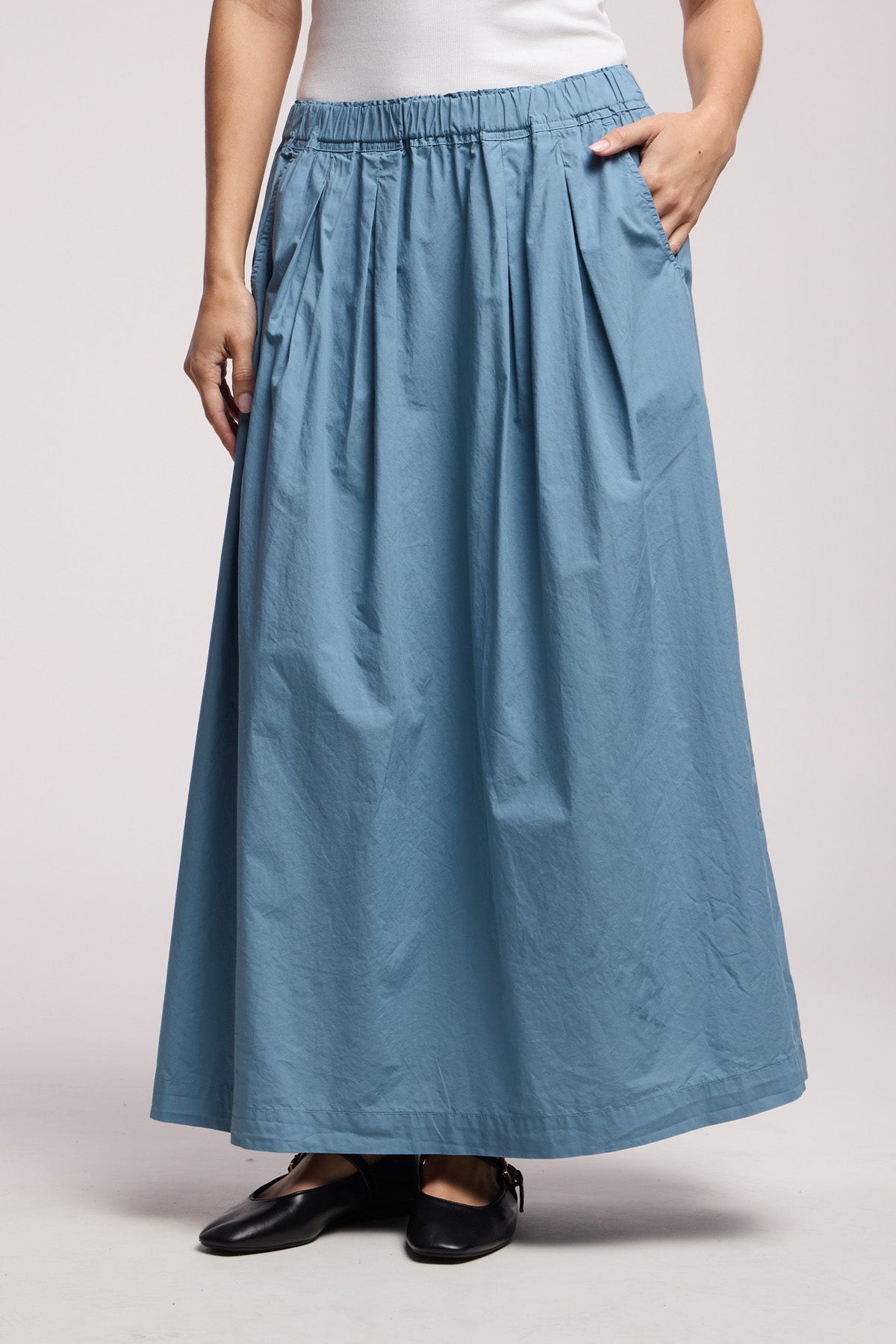 A person wearing the CHESSA SKIRT by Velvet by Graham & Spencer in light blue with pockets and black flat shoes, standing against a plain background.