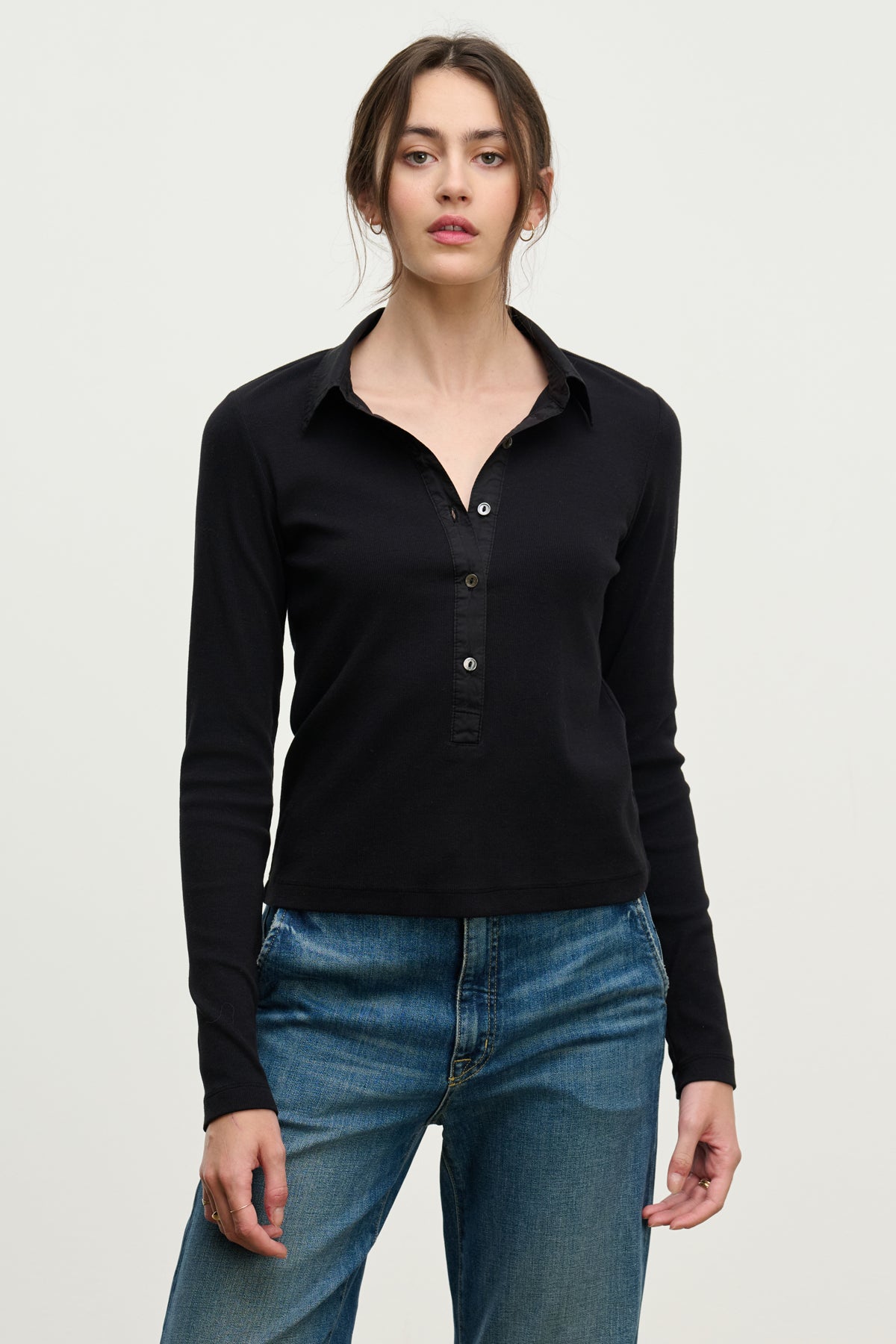 A woman faces forward in the ARVINE SHIRT by Velvet by Graham & Spencer—a black ribbed top with a cotton poplin collar and buttons—paired with blue jeans against a plain light background.