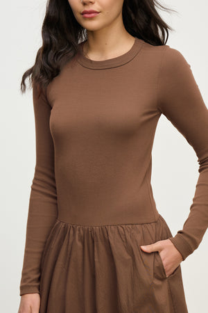 A woman models the DOLCE DRESS by Velvet by Graham & Spencer—a ribbed cotton dress with long sleeves, fitted top, and gathered skirt—against a plain light background.