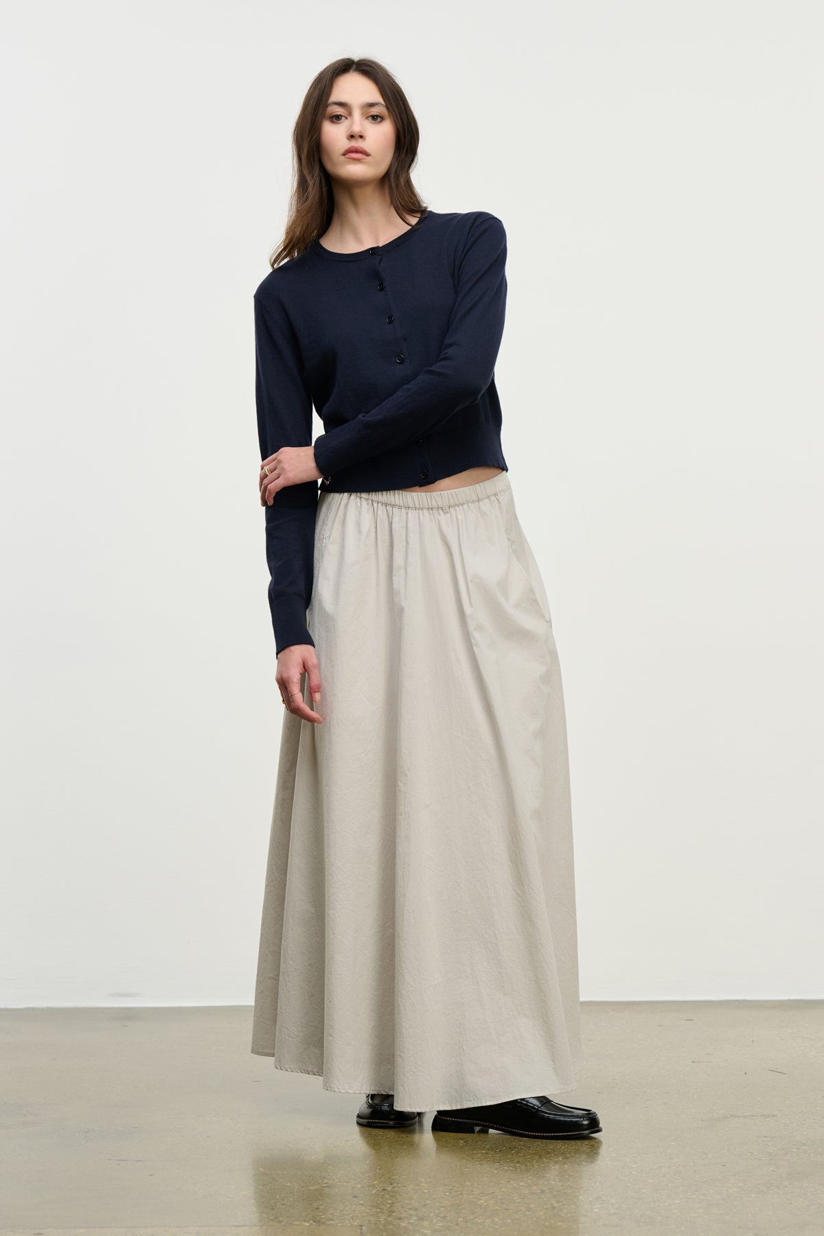 A woman stands indoors against a plain light background wearing black shoes, a navy long-sleeve top, and the FILLA SKIRT by Velvet by Graham & Spencer—a light beige cotton poplin skirt with an elastic waist.-39800308007105