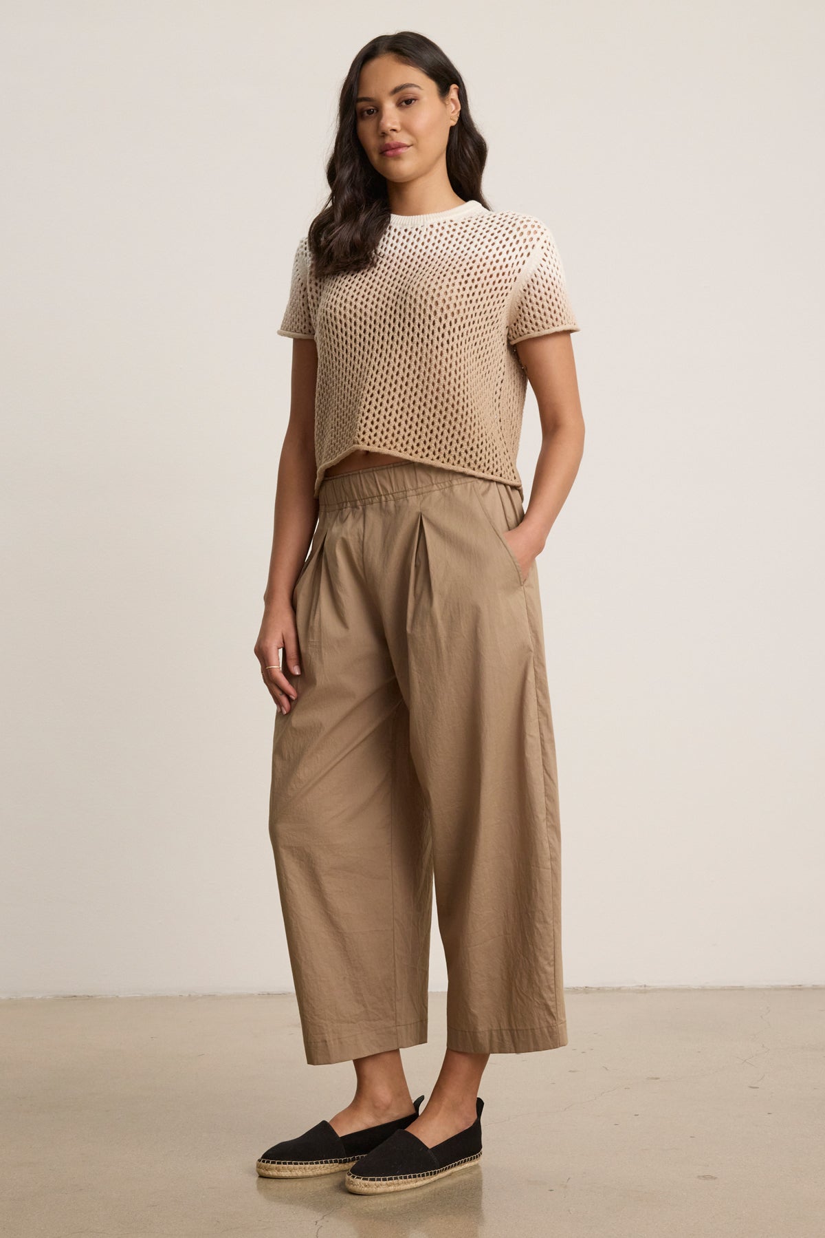 A woman stands against a plain background wearing a beige short-sleeve knit top, black espadrilles, and the SOPHIA PANT by Velvet by Graham & Spencer—cropped balloon pants in cotton poplin with an elastic waist, her hands in her pockets.-40030496227521