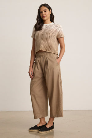 A woman stands against a plain background wearing a beige short-sleeve knit top, black espadrilles, and the SOPHIA PANT by Velvet by Graham & Spencer—cropped balloon pants in cotton poplin with an elastic waist, her hands in her pockets.