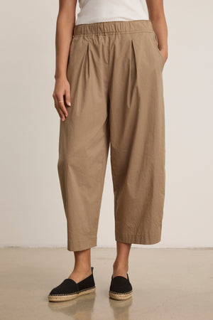 A person stands against a plain background wearing Velvet by Graham & Spencer’s SOPHIA PANT in beige with a relaxed cropped silhouette, paired with a white top and black espadrilles.