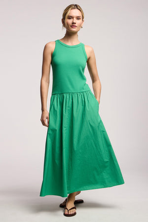 A person stands against a plain background wearing the ROMILLY DRESS by Velvet by Graham & Spencer, featuring a green ribbed bodice with a cotton poplin skirt, paired with brown sandals.