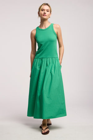 A woman wears the ROMILLY DRESS by Velvet by Graham & Spencer, featuring a sleeveless green fitted ribbed bodice and matching ankle-length skirt, standing against a plain light background.