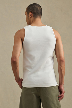 A man with short hair stands with his back to the camera, wearing the Velvet by Graham & Spencer CARLOS TANK in white and olive green shorts against a plain background.