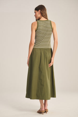 A woman faces away, wearing the Velvet by Graham & Spencer ROMINA DRESS—a sleeveless, green and white striped cotton rib dress styled as a midi skirt—paired with brown heeled sandals against a plain background.