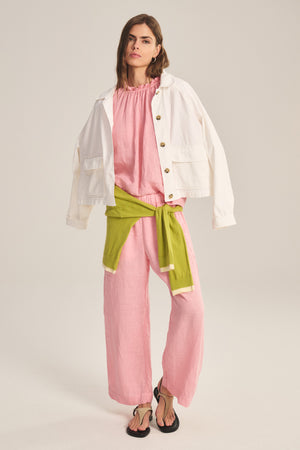 A person stands against a plain background wearing Velvet by Graham & Spencer's LOLA LINEN PANT—relaxed, straight-leg linen pants with an elastic waistband—paired with a white jacket, pink blouse, green sweater at the waist, and black sandals.