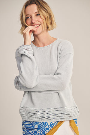 A woman with a short blonde bob smiles with her hand near her mouth, wearing the ROSALYN SWEATER by Velvet by Graham & Spencer—a light Pima cotton knit with pointelle detailing—against a neutral background.