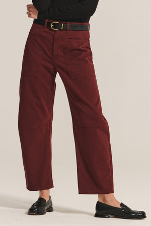 Person wearing Velvet by Graham & Spencer's BRYLIE SANDED TWILL UTILITY PANT—high-waisted, wide-leg maroon cotton trousers with patch pockets—styled with a black belt and loafers against a plain background.