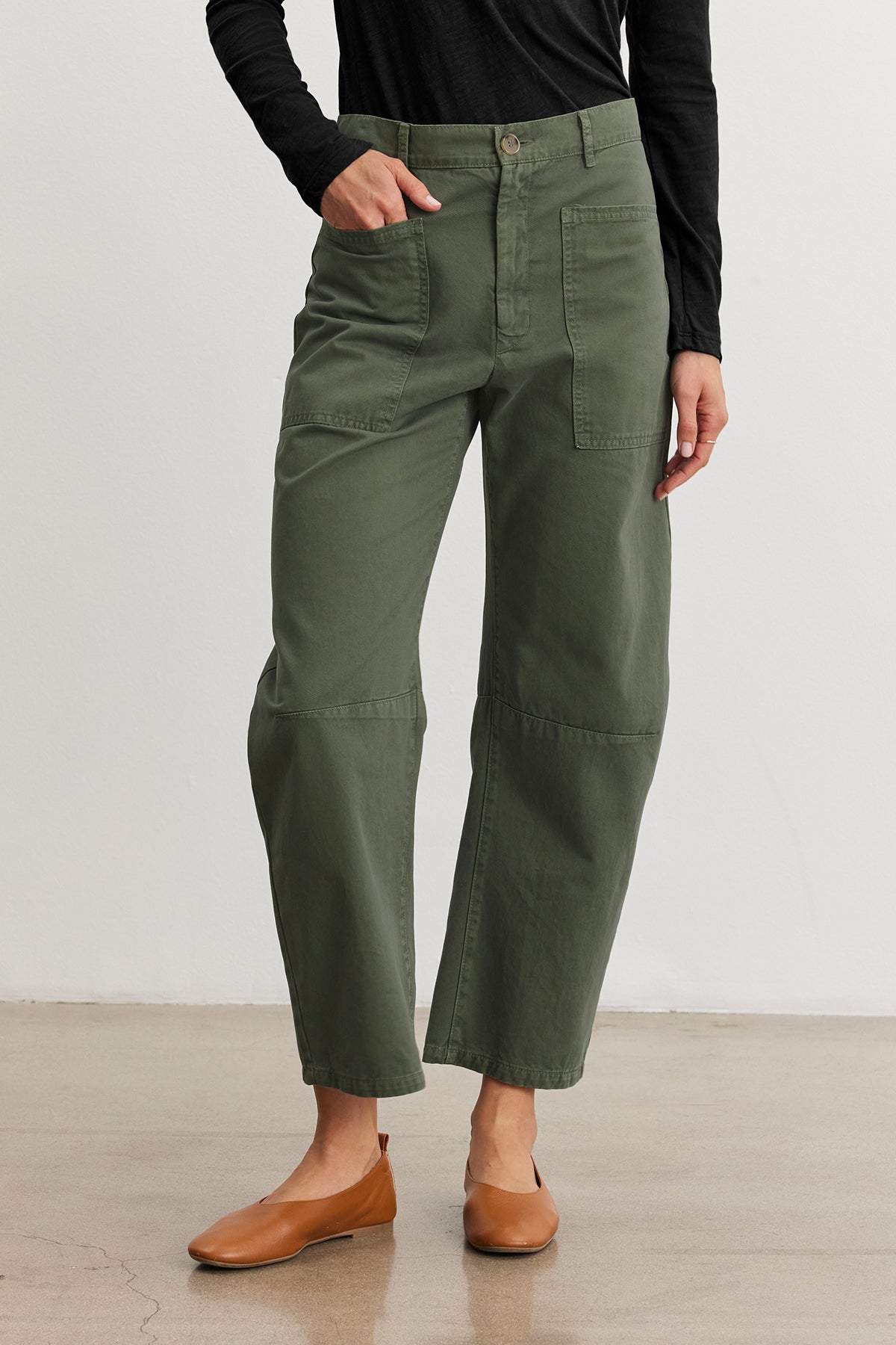   On a plain floor, someone wears the BRYLIE SANDED TWILL UTILITY PANT by Velvet by Graham & Spencer, featuring green high-waisted cotton twill, paired with a sleek black long-sleeve top. 