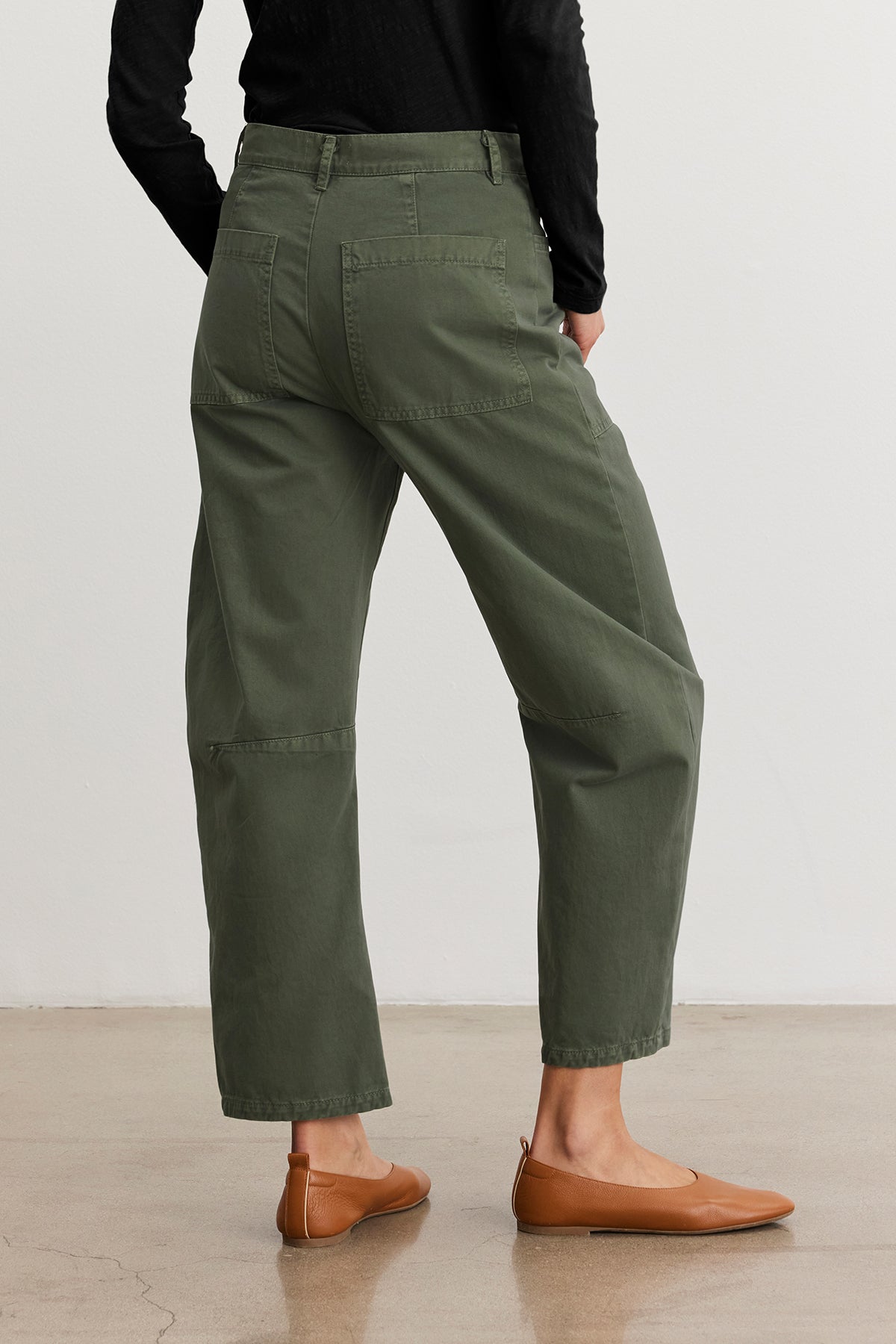 A person in Velvet by Graham & Spencer's Brylie Sanded Twill Utility Pant stands on a polished floor in brown flats, facing away.-38662647152833