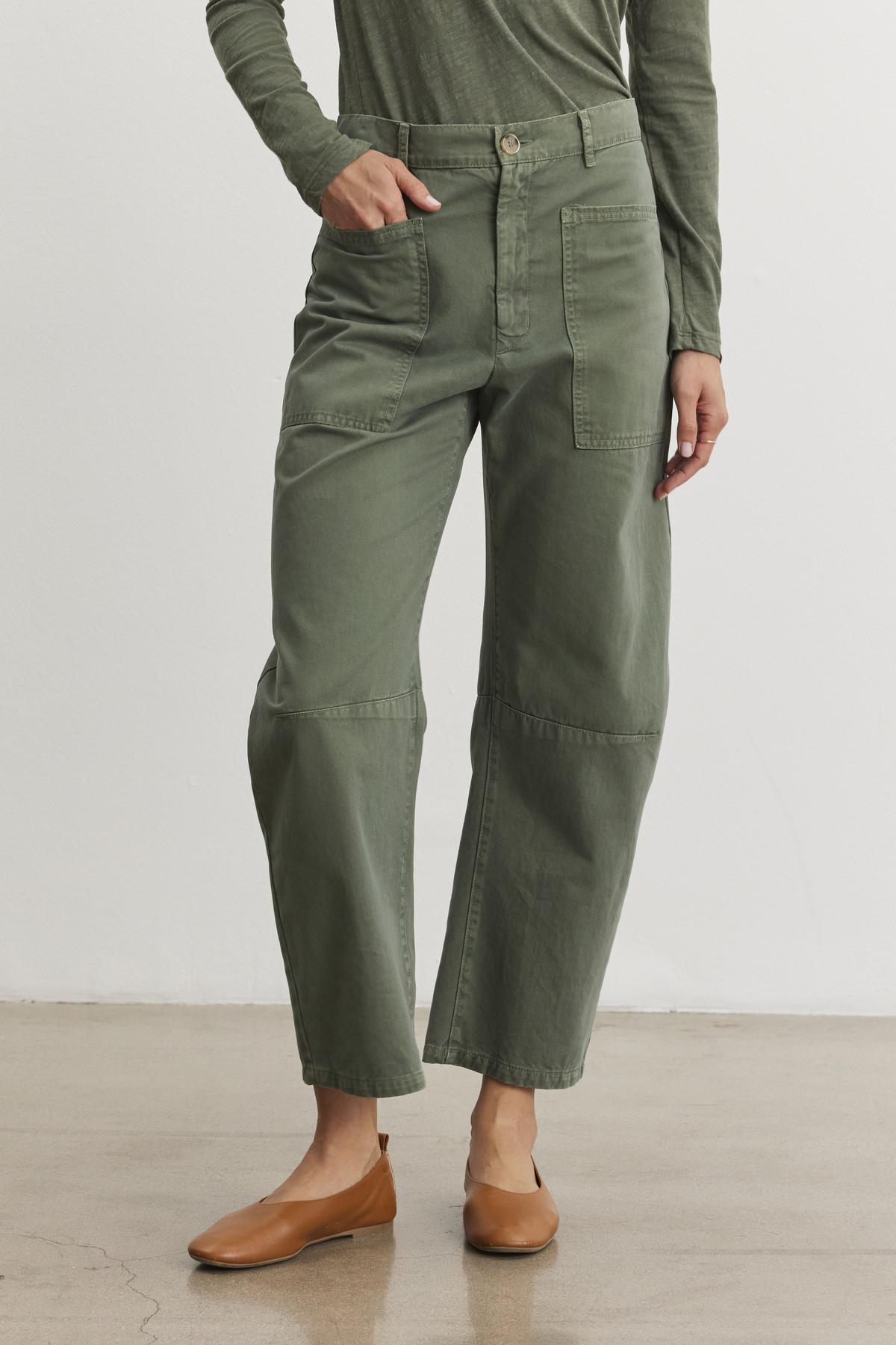 Someone in a green long-sleeve shirt and Velvet by Graham & Spencer's BRYLIE SANDED TWILL UTILITY PANT stands on a polished concrete floor, wearing tan flat shoes.-38512044310721