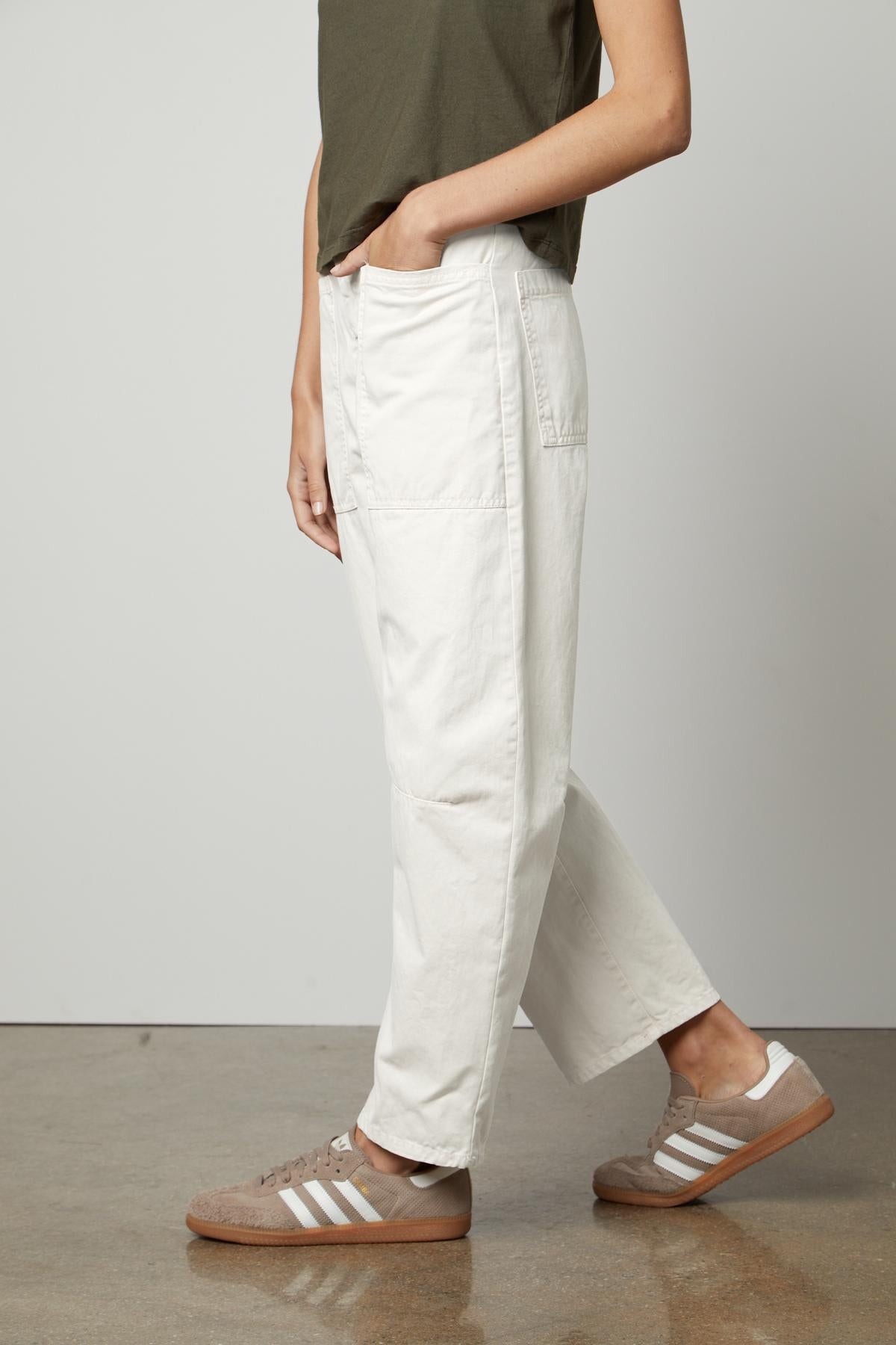   A person wearing Velvet by Graham & Spencer's BRYLIE SANDED TWILL UTILITY PANT and brown sneakers stands in a neutral pose against a gray background. 