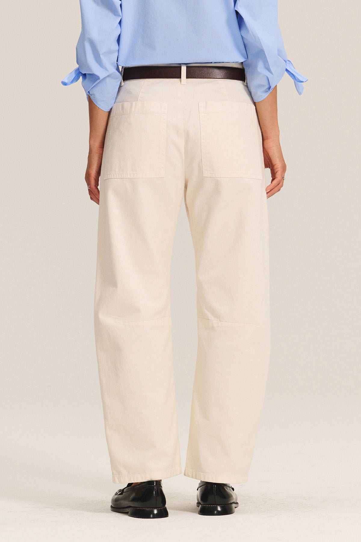 Person shown from the back wearing the BRYLIE SANDED TWILL UTILITY PANT by Velvet by Graham & Spencer in beige, styled with a light blue shirt, dark belt, and black shoes. Features include utilitarian patch pockets and cotton twill fabric.-40333256360129