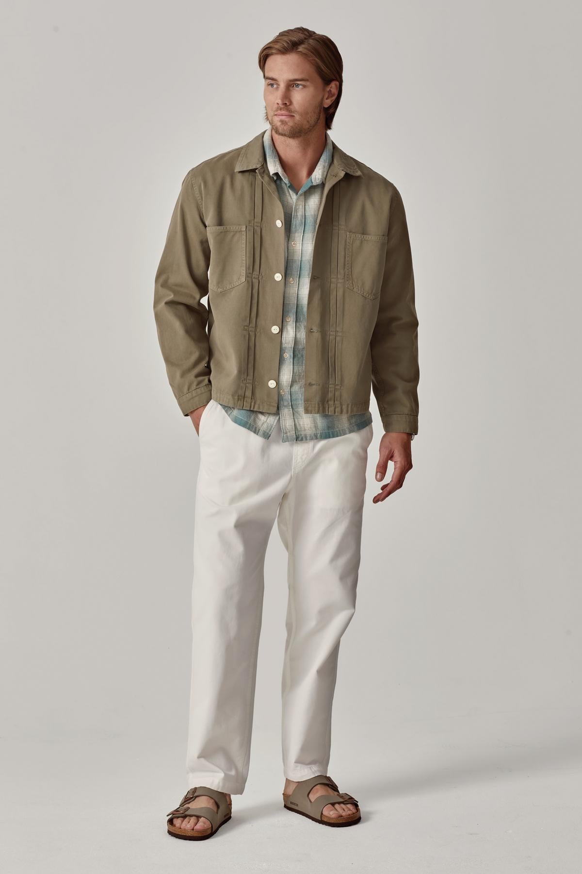   A man in a casual outfit featuring a green jacket, plaid shirt, BRANSON PANT by Velvet by Graham & Spencer with an elastic drawstring waist, and brown sandals. 
