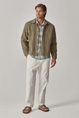 A man in a casual outfit featuring a green jacket, plaid shirt, BRANSON PANT by Velvet by Graham & Spencer with an elastic drawstring waist, and brown sandals.
