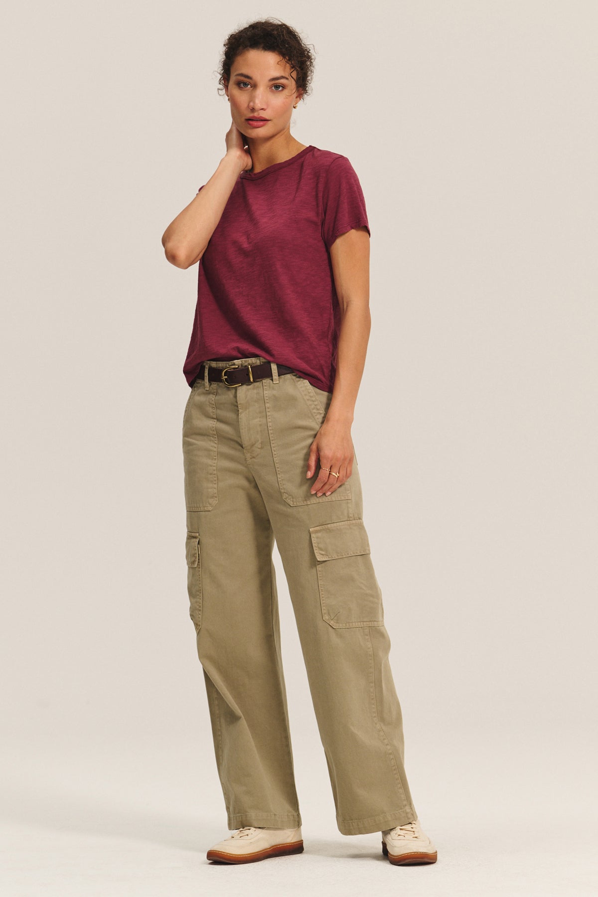   A person stands against a plain background wearing the MARIKA TEE by Velvet by Graham & Spencer in a relaxed, boxy fit maroon cotton slub, paired with khaki cargo pants with pockets, a belt, and cream sneakers. 