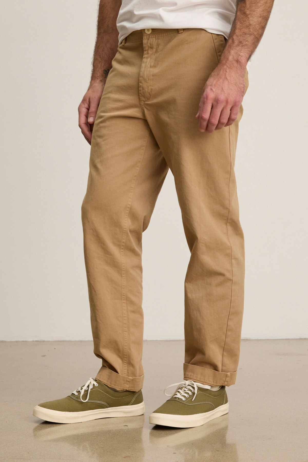 Indoors on a polished floor, a person wears Velvet by Graham & Spencer's LENNOX PANT—relaxed fit tan cotton twill pants—paired with olive green sneakers with white soles, ideal for everyday style.-39446033563841