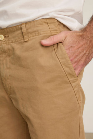 A person wearing Velvet by Graham & Spencer’s LENNOX PANT in relaxed fit tan cotton twill and a white shirt has their right hand in the pants pocket.