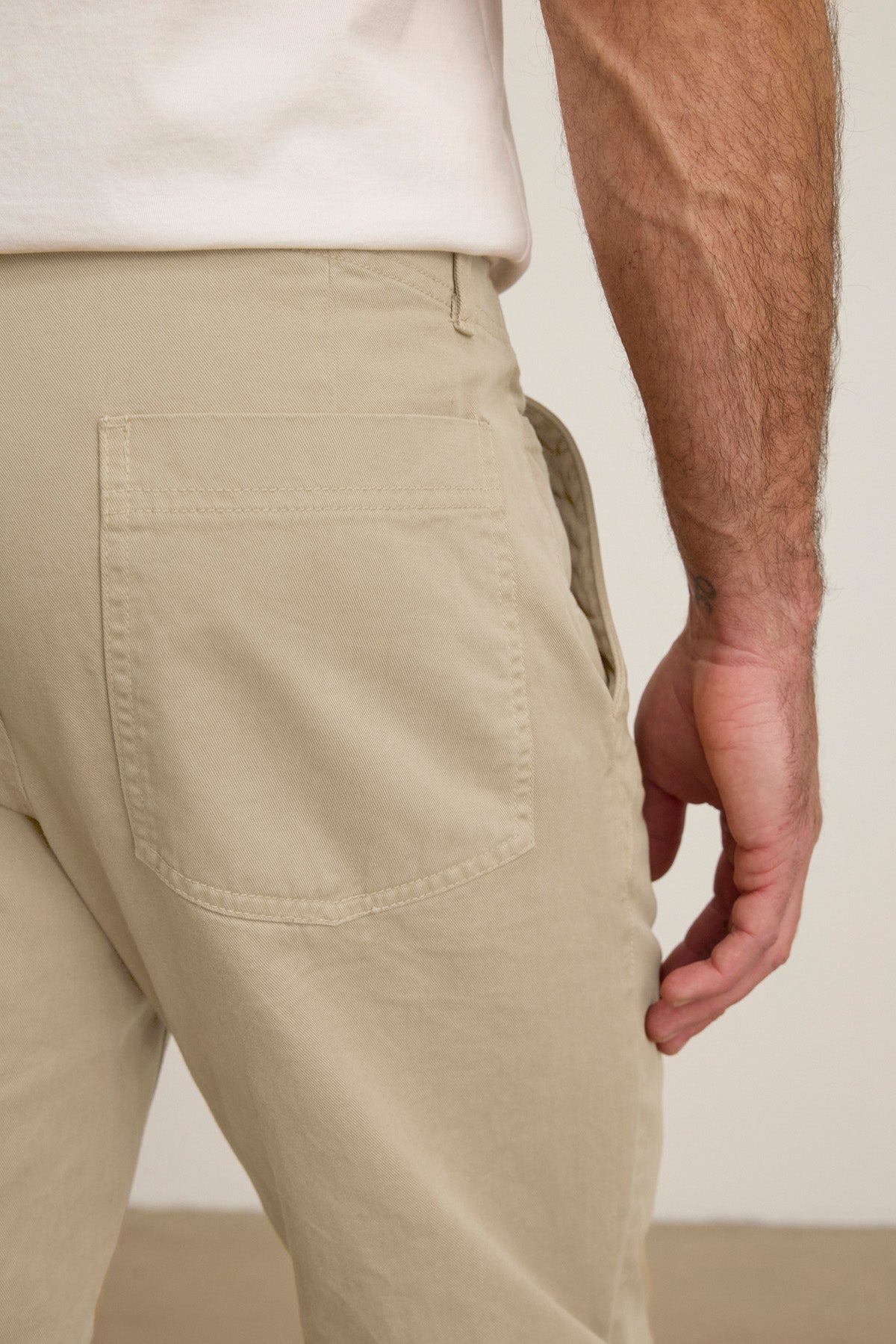 Close-up of a person in LENNOX PANT by Velvet by Graham & Spencer—beige cotton twill with a white shirt, showcasing the back pocket and right arm. Ideal for everyday wear.-40850767216833